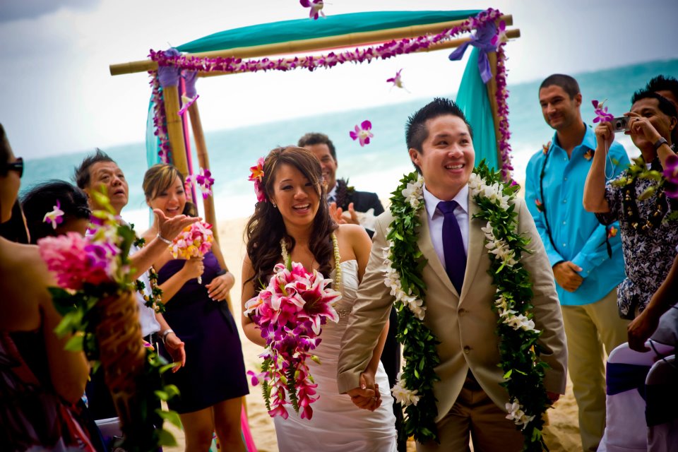 orchid purple flowers in the air as the newlyweds walk down the aisle sandy way